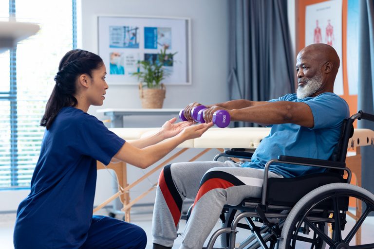 Physiotherapeutin hilft Patient im Rollstuhlt beim Trainieren mit Gewichten