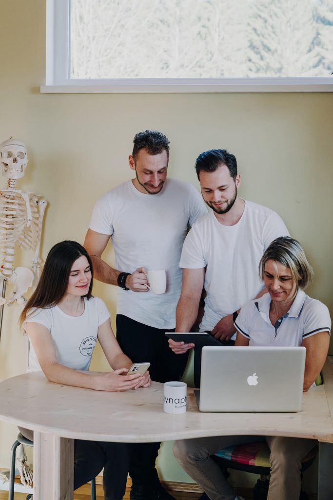 Zwei Männer und zwei Frauen in weißen T-Shirts blicken auf MacBook Bildschirm