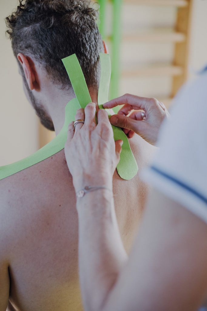 Therapeutin klebt Kinesio-Tape auf Nacken eines Patienten