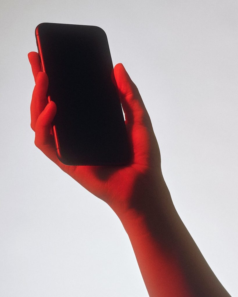 Hand mit schwarzem Smartphone in rotem Licht