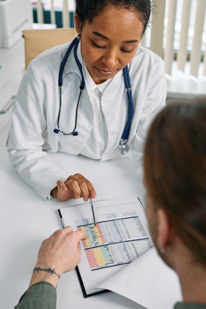 Ärztin in weißem Kittel zeigt Patient mit Stift auf Papier Untersuchungsergebnisse