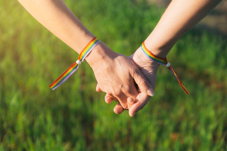 Zwei Menschen reichen sich die Hände mit Regenbogenarmbändern auf Wiese